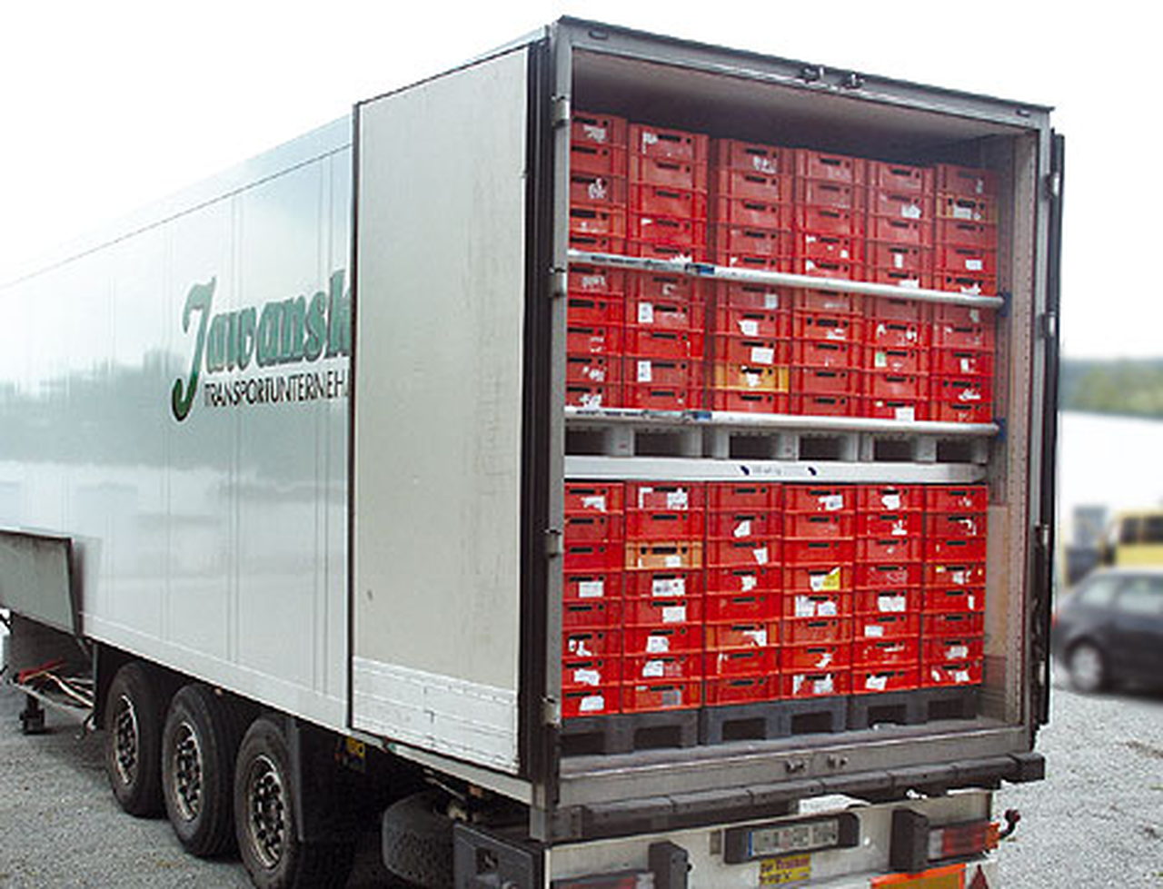 Ein LKW-Anhänger mit offener Hecktür, gefüllt mit roten Kisten auf Paletten.